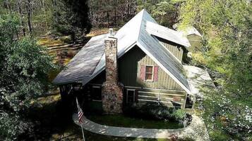 A rustic cabin with a stone chimney, a red window, and a flagpole with an American flag.