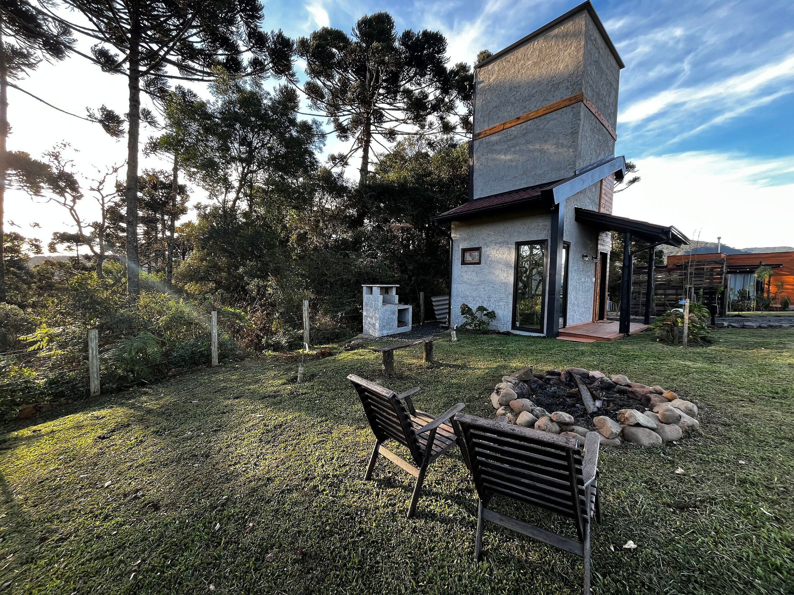 Una casa moderna de dos pisos con un patio, una fogata y un banco de madera.