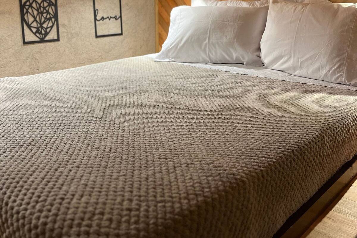 A bedroom with a wooden ceiling, a bed with white bedding, and two wall decorations.