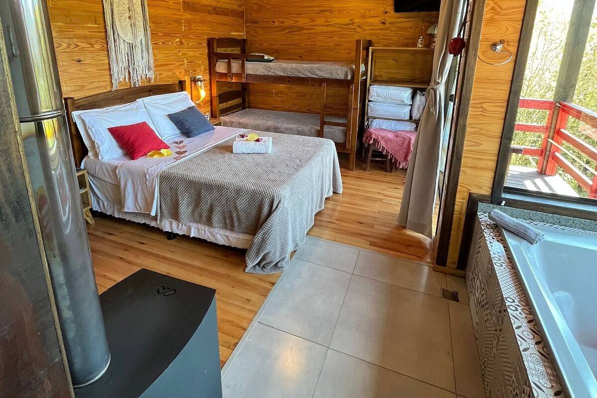 A wooden cabin interior with a bunk bed, a small table, a heater, and a window with a view.