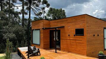 A modern wooden house with a patio, a bench, and potted plants.