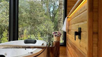A modern bathroom with a freestanding bathtub, a wooden vanity, and a large window offering a view of trees.