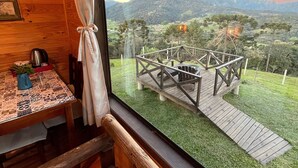 A wooden cabin interior with a large window overlooking a deck and a mountainous landscape. - Chalés Solar da Montanha Urubici (Urubici)