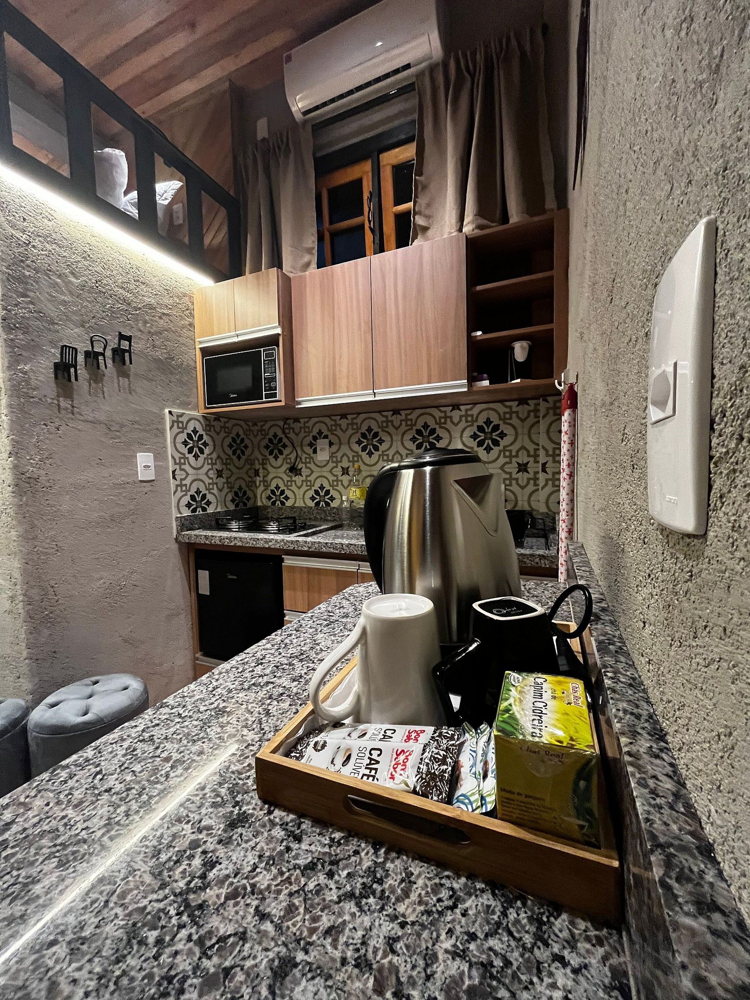Una cocina compacta con microondas, hervidor y una bandeja con alimentos.