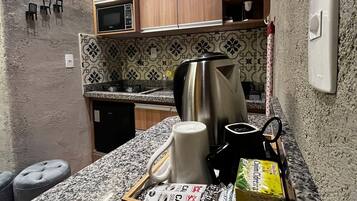 Una cocina compacta con microondas, hervidor y una bandeja con alimentos.