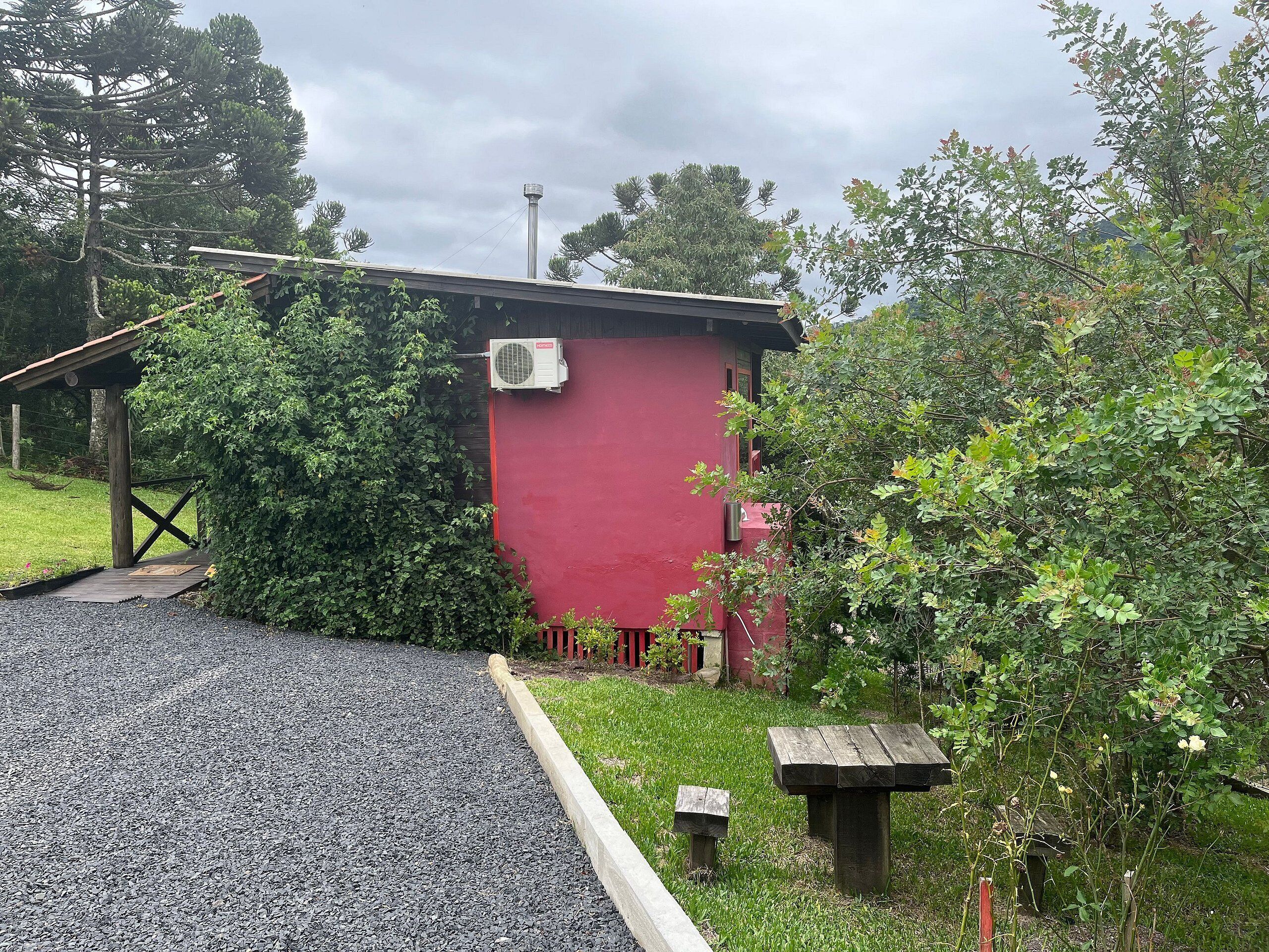 Un edificio rojo con camino de grava, banco de madera y pequeño jardín.