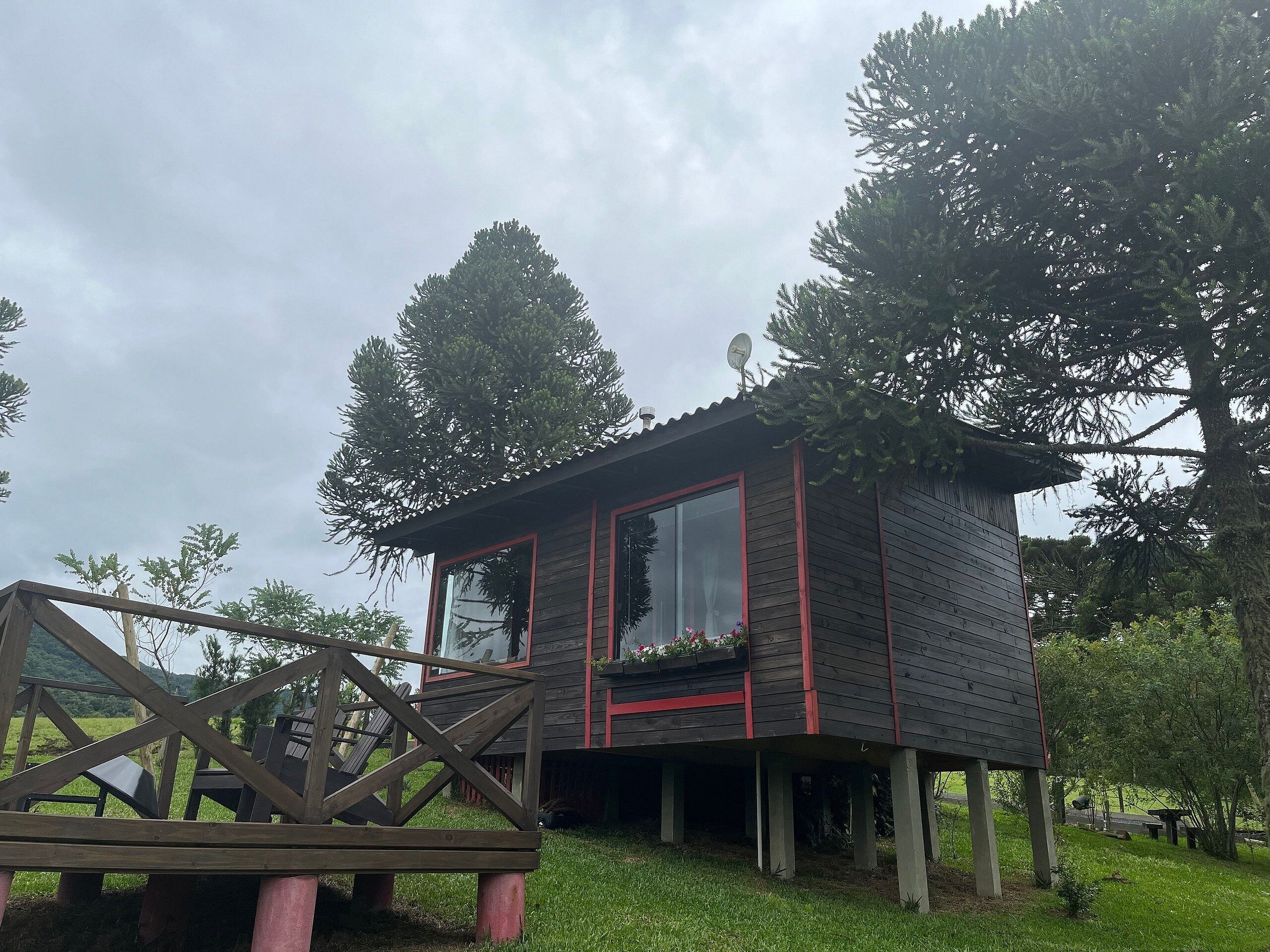 Uma cabana de madeira com janela emoldurada em vermelho, um deck e uma antena parabólica.