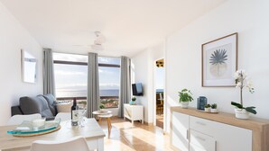 A modern living room with a large window, a dining area, and a kitchen. - Playa La Arena with pool and privat parking (Santiago del Teide)