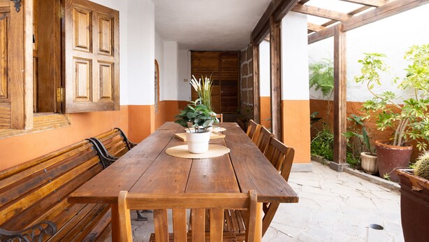 Una mesa de comedor de madera con sillas, una planta en maceta y una puerta de madera en una habitación con paredes blancas y anaranjadas.