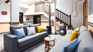 Un amplio salón con un conjunto de sofás grises, una mesita redonda y una escalera que lleva a un nivel superior.