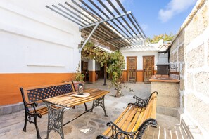 Eine Terrasse im Freien mit einem Holztisch und Bänken, einer Pergola und einer Steinmauer.