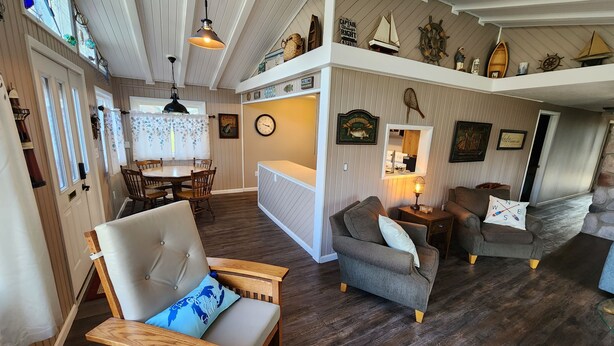 Un intérieur chaleureux comprenant un coin repas, un salon avec un canapé et des fauteuils, et une décoration sur le thème de la marine.