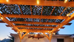 Une terrasse extérieure dotée d’un foyer, d’une pergola en bois et de guirlandes lumineuses.