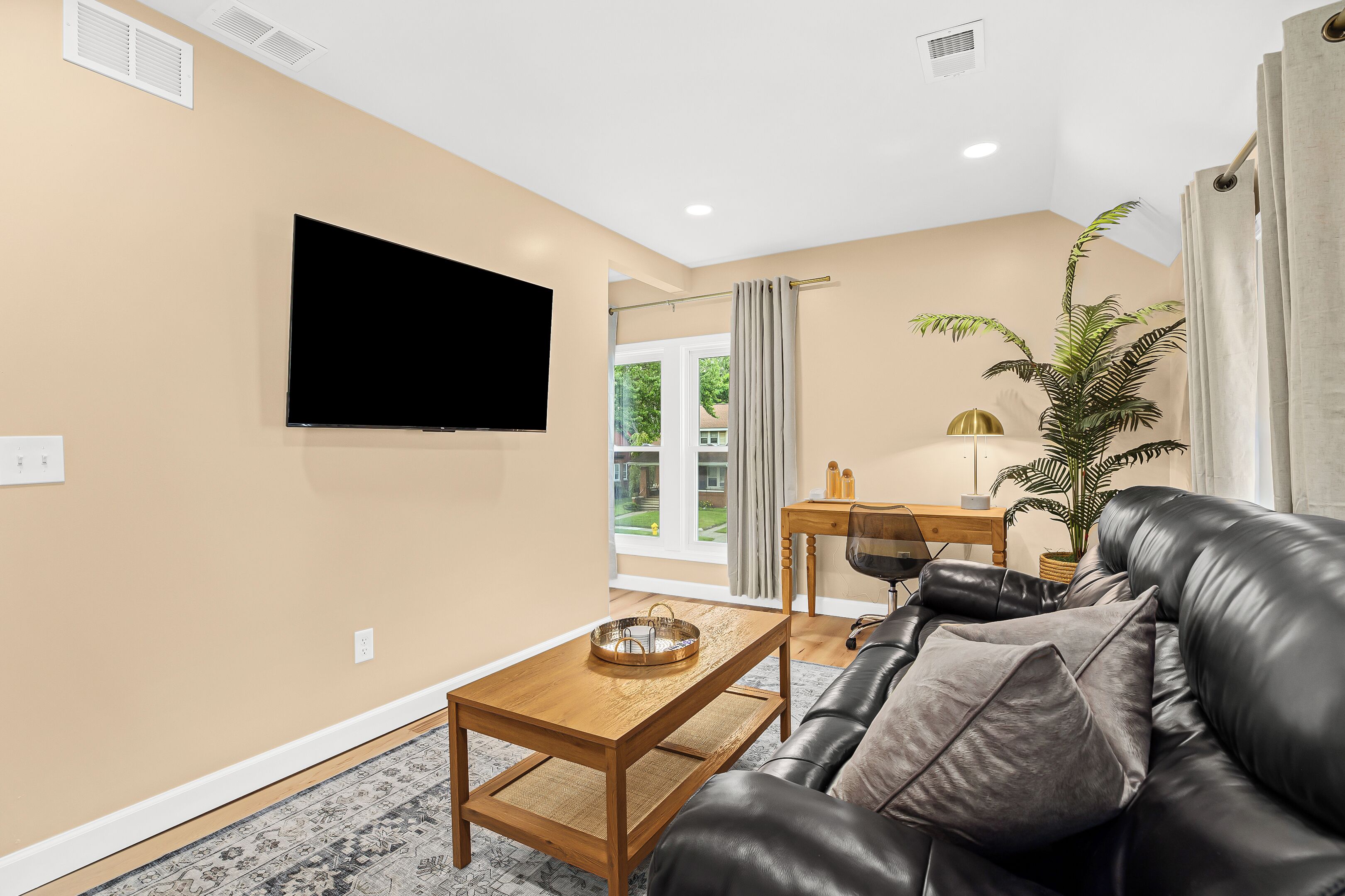 A living room with a leather sofa, a wooden coffee table, a flat-screen TV, and a potted plant.