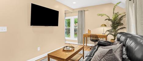 A living room with a leather sofa, a wooden coffee table, a flat-screen TV, and a potted plant.