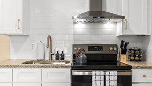 A modern kitchen with white cabinetry, a stainless steel range hood, a kettle on the stove, and a knife block on the countertop.
