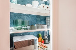 A kitchen with a blue patterned backsplash, white shelves, and various kitchen items including a blender, a pineapple, and a fruit tray. - Perfect Private Getaway in Princeville! (Princeville)