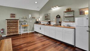 Una cocina con armarios blancos, suelo de madera, microondas, cafetera y refrigerador.