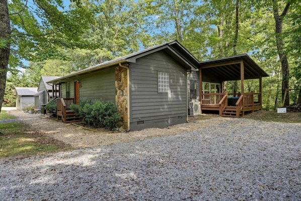A cabin with a covered porch, a small attached shed, and a gravel driveway.