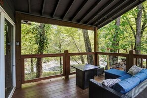 A covered outdoor deck with a wooden railing, a sofa, and a table.