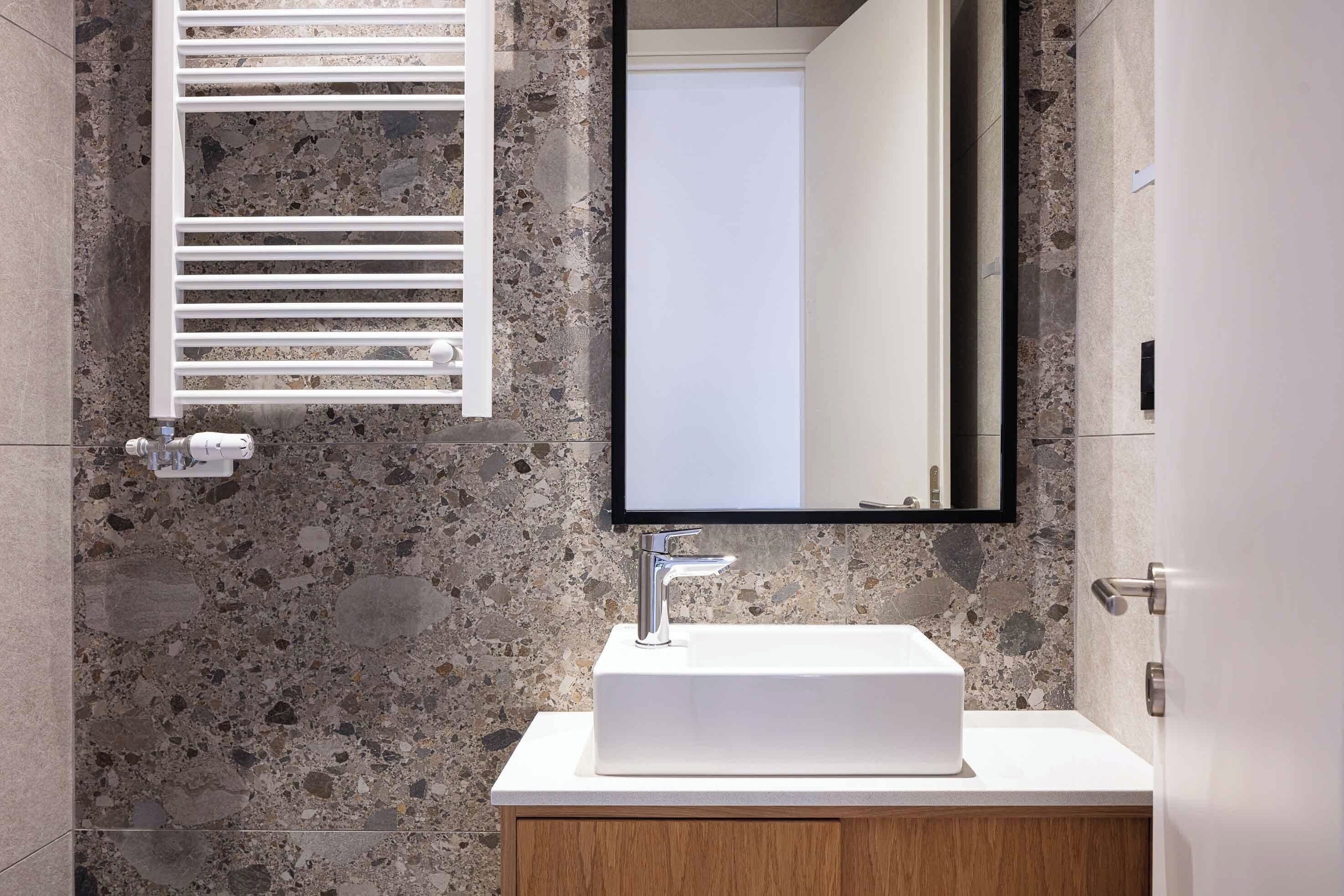 Un baño con lavamanos blanco, espejo y toallero.