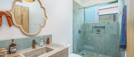 Een moderne badkamer met een grote spiegel, een wastafel met toiletartikelen en een douchecabine van glas.