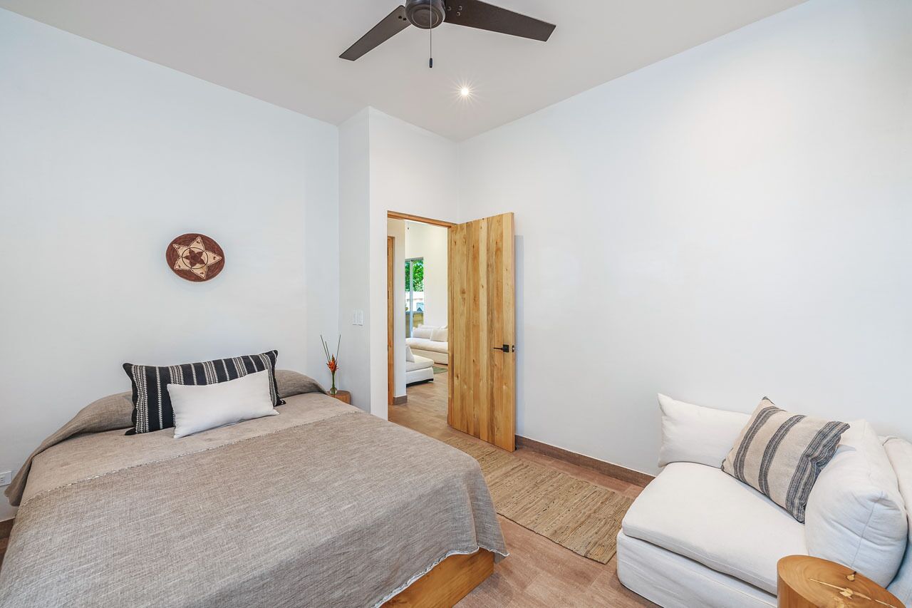 Une chambre à coucher avec un lit, un ventilateur de plafond, une porte en bois et un canapé blanc.