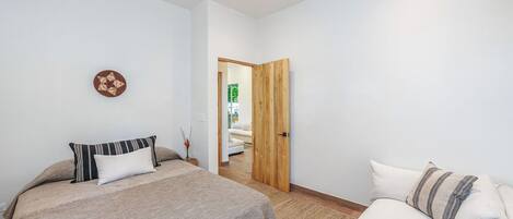 Une chambre à coucher avec un lit, un ventilateur de plafond, une porte en bois et un canapé blanc.