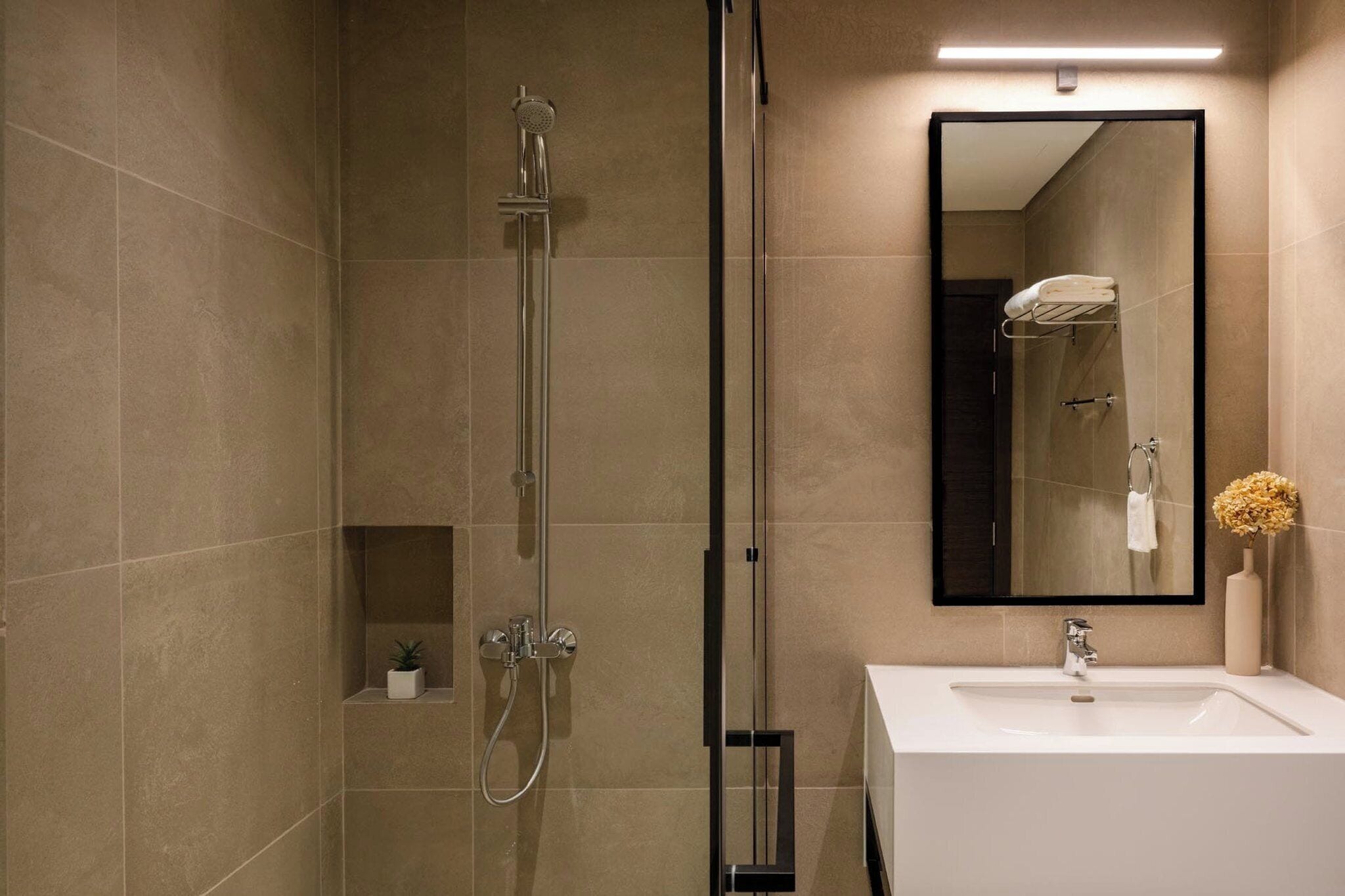 Ein modernes Badezimmer mit einer gläsernen Dusche, einem weißen Waschbecken und einem großen Spiegel.