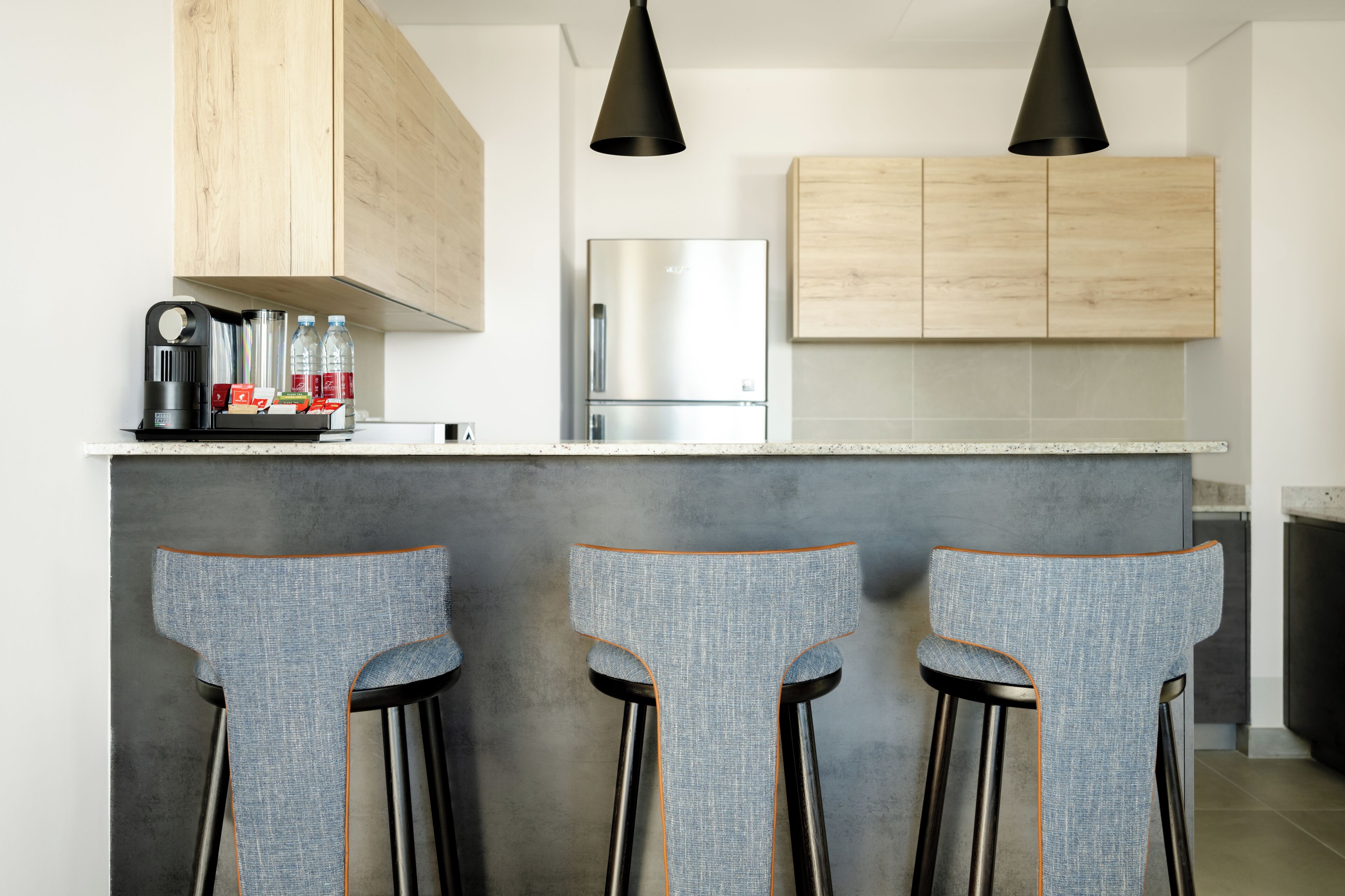 A modern kitchen with wooden cabinets, a stainless steel refrigerator, and a bar area with three stools.