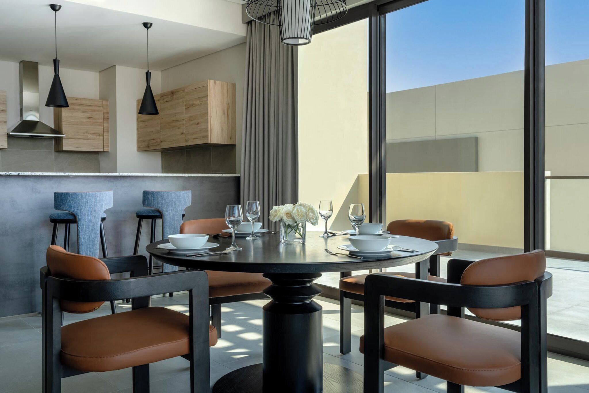 A modern dining area with a round table, six chairs, and a vase of white flowers.