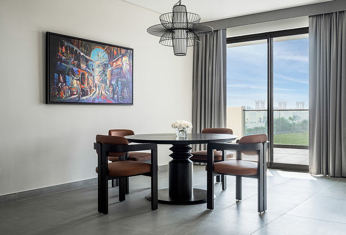 Un comedor moderno con una mesa redonda, seis sillas, un cuadro abstracto grande y vistas al exterior a través de amplios ventanales.