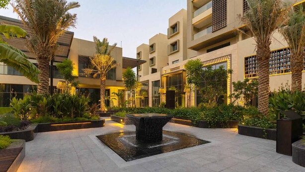 A courtyard with a central water feature, surrounded by palm trees and greenery, with modern buildings in the background. - Fraser Suites AL Liwan (Hamala)