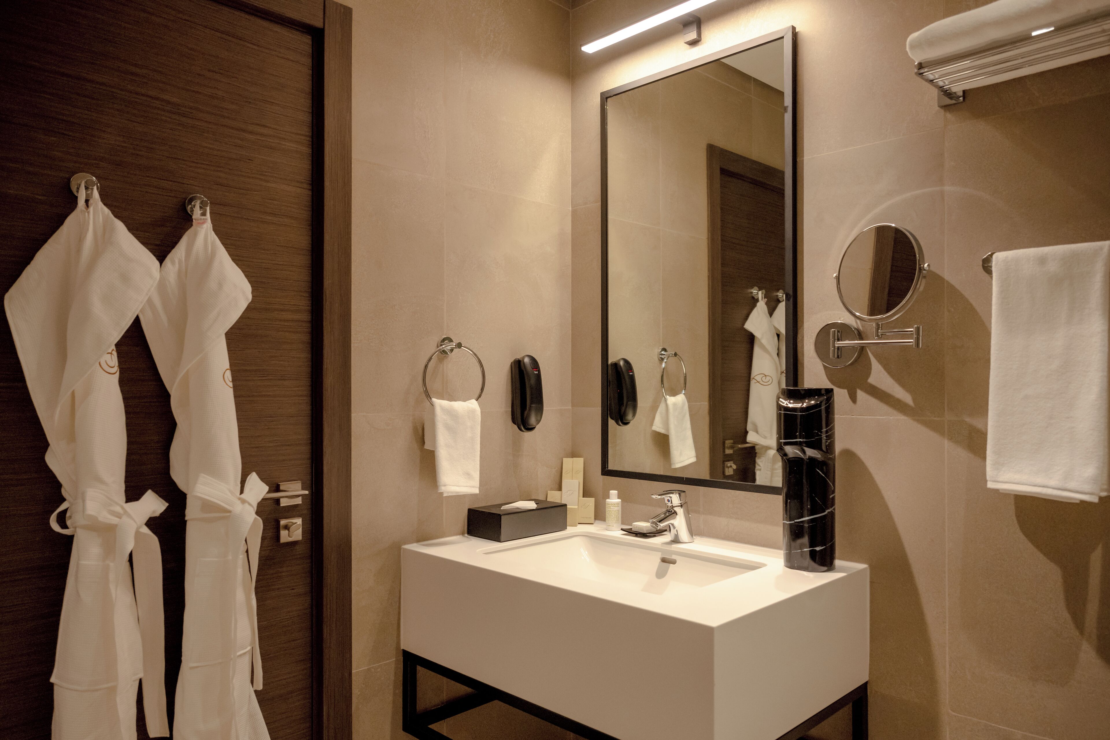 A modern bathroom with a large mirror, a white sink, and two white towels hanging on hooks.