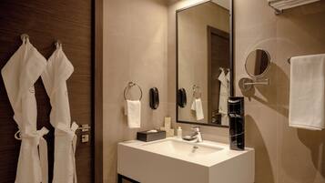 A modern bathroom with a large mirror, a white sink, and two white towels hanging on hooks.
