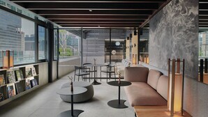 A modern lounge area with a sofa, round tables, and a bookshelf with books. - 21 Carpenter, Singapore, a Member of Design Hotels (Singapore)