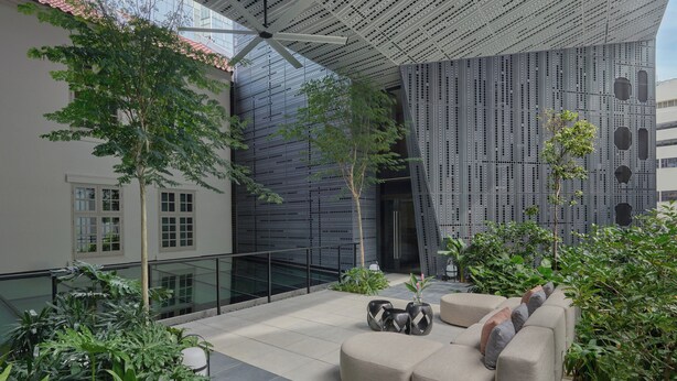 An indoor courtyard with a modern design, featuring a seating area with sofas and planters, a glass railing, and a unique perforated ceiling structure. - 21 Carpenter, Singapore, a Member of Design Hotels (Singapore)
