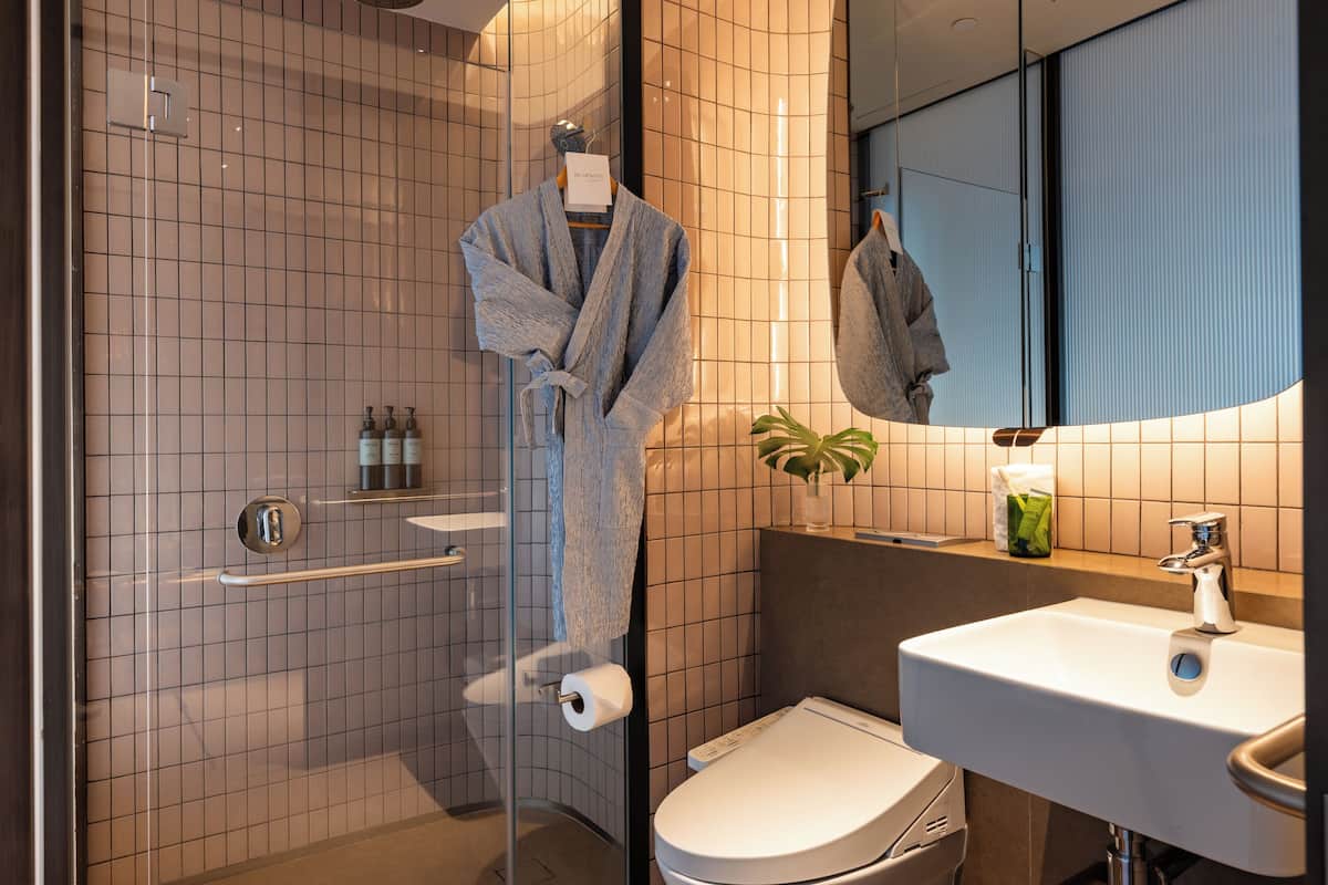 A modern bathroom with a glass shower enclosure, a white toilet, a sink with a mirror, and a robe hanging on a rack.
