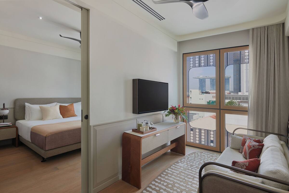 A modern hotel room with a bed, a TV, a desk, and a view of the cityscape.