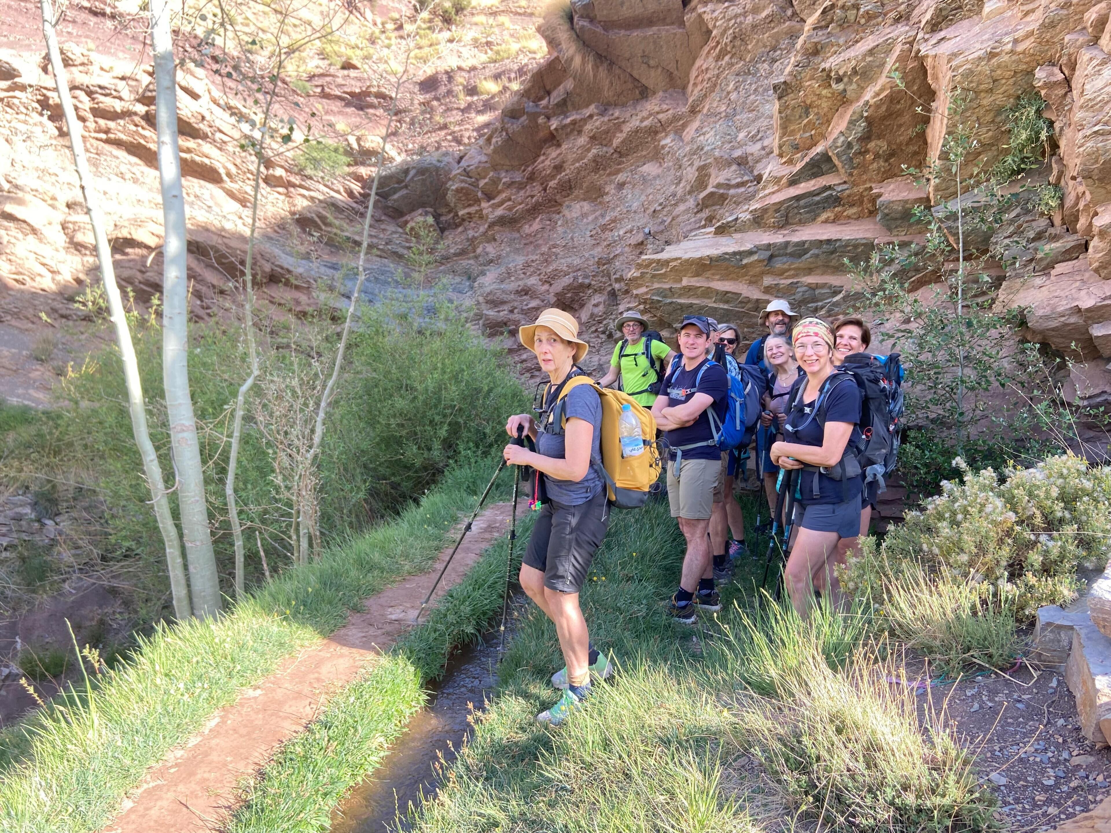 A group of hikers on a rocky trail with a narrow path and vegetation on either side.