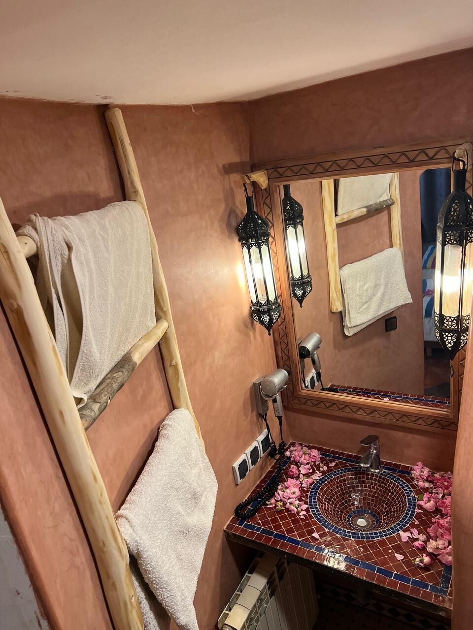 Un baño con un toallero de madera, un espejo con una toalla y un lavamanos con diseño de azulejos.