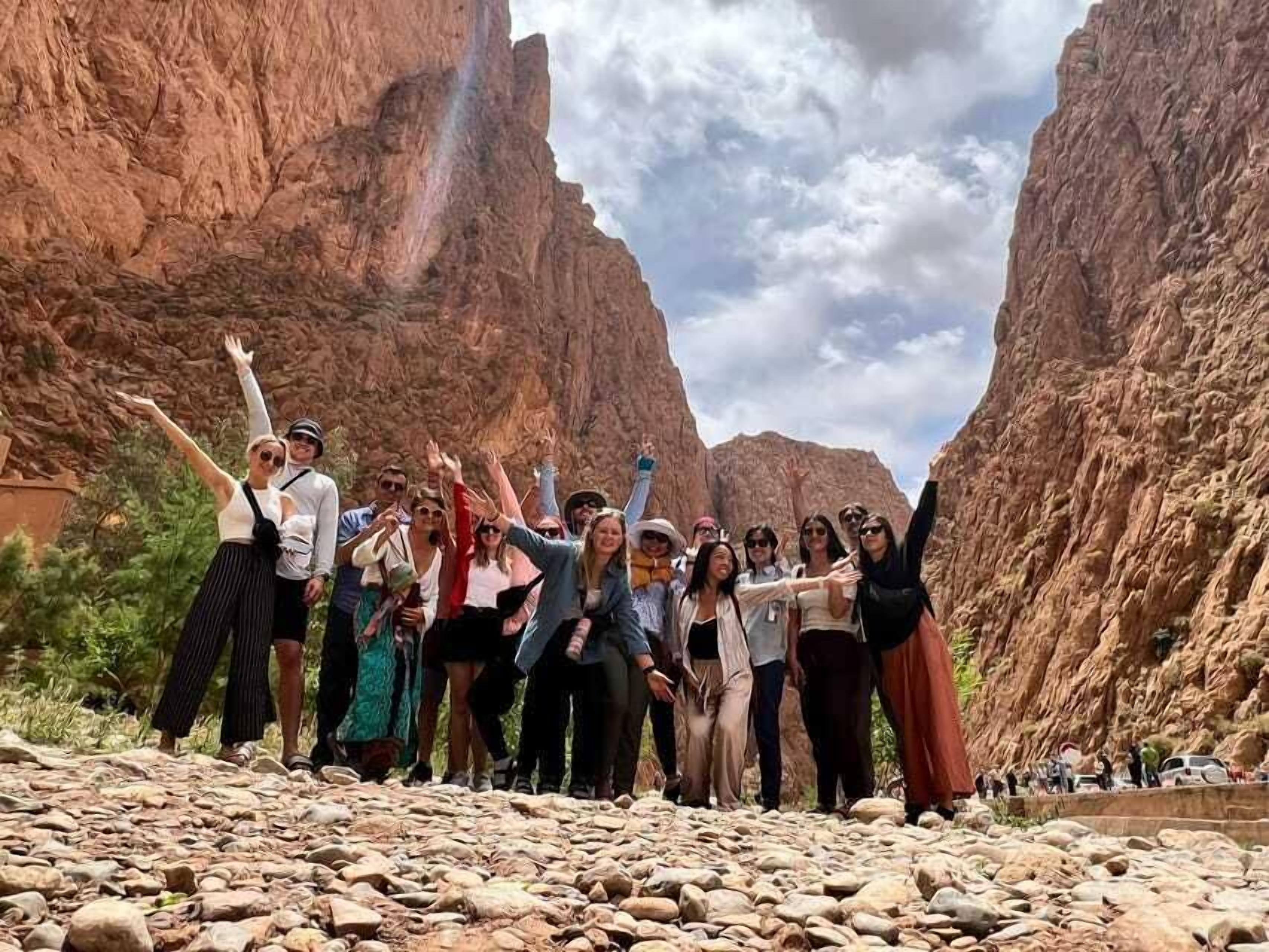 A group of people standing in a canyon with rocky terrain and a river.