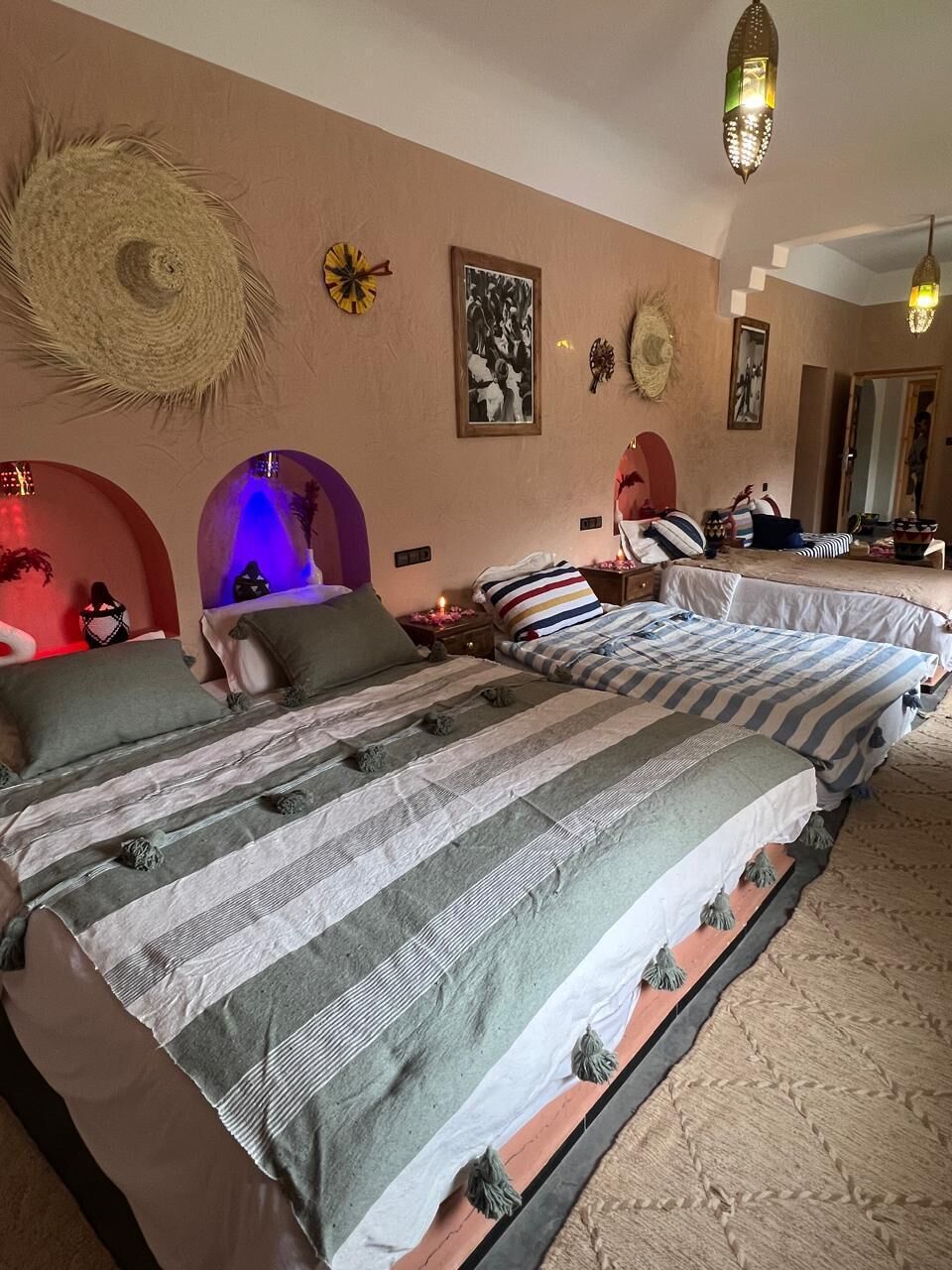 Habitación de hotel con dos camas, un adorno de pared tejido grande y un candelabro.
