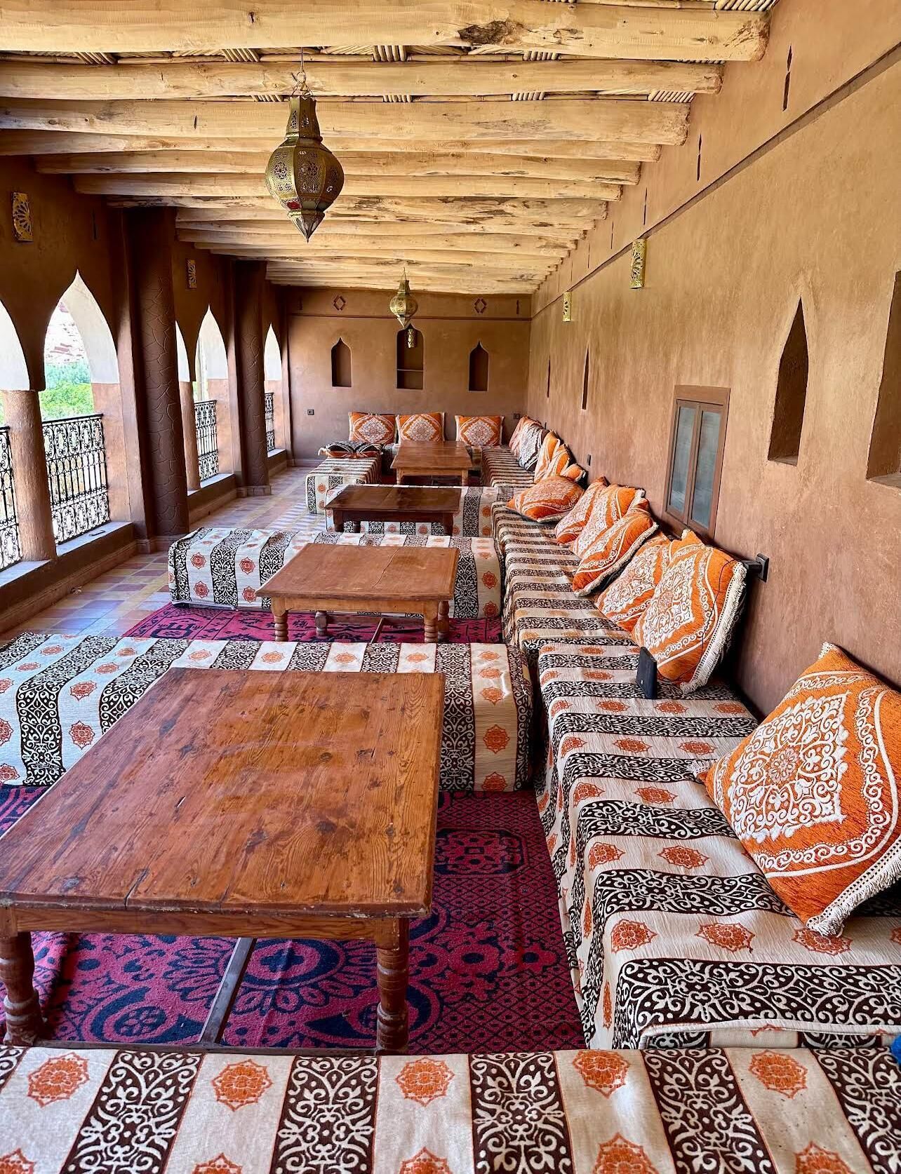 Un interior tradicional con una larga hilera de sofás y mesas, ventanas de arco y alfombras estampadas.