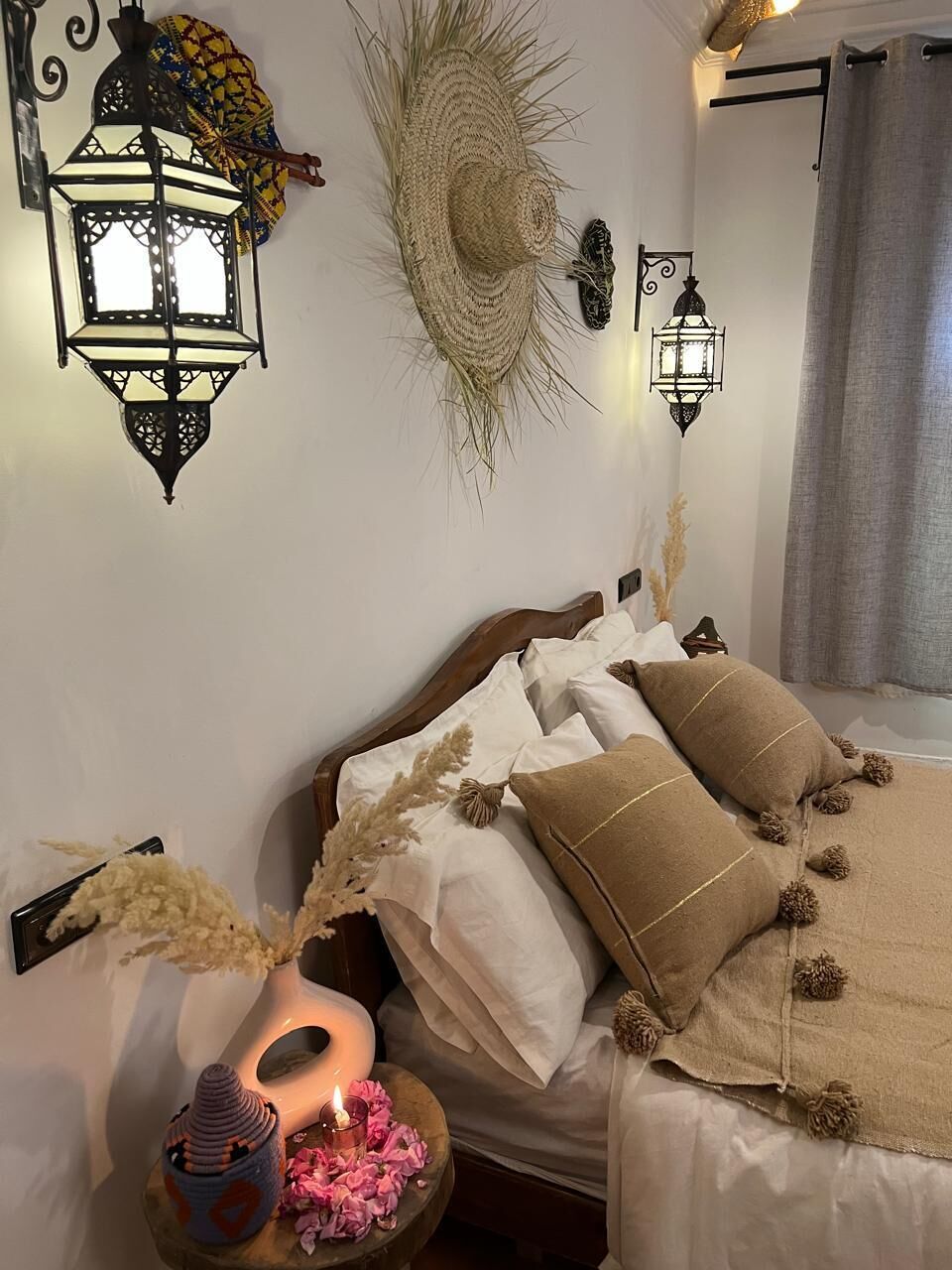 Ein Schlafzimmer mit einem Bett, dekorativen Wandleuchten, einem gewebten Wandbild und einem Nachttisch mit einer Kerze.