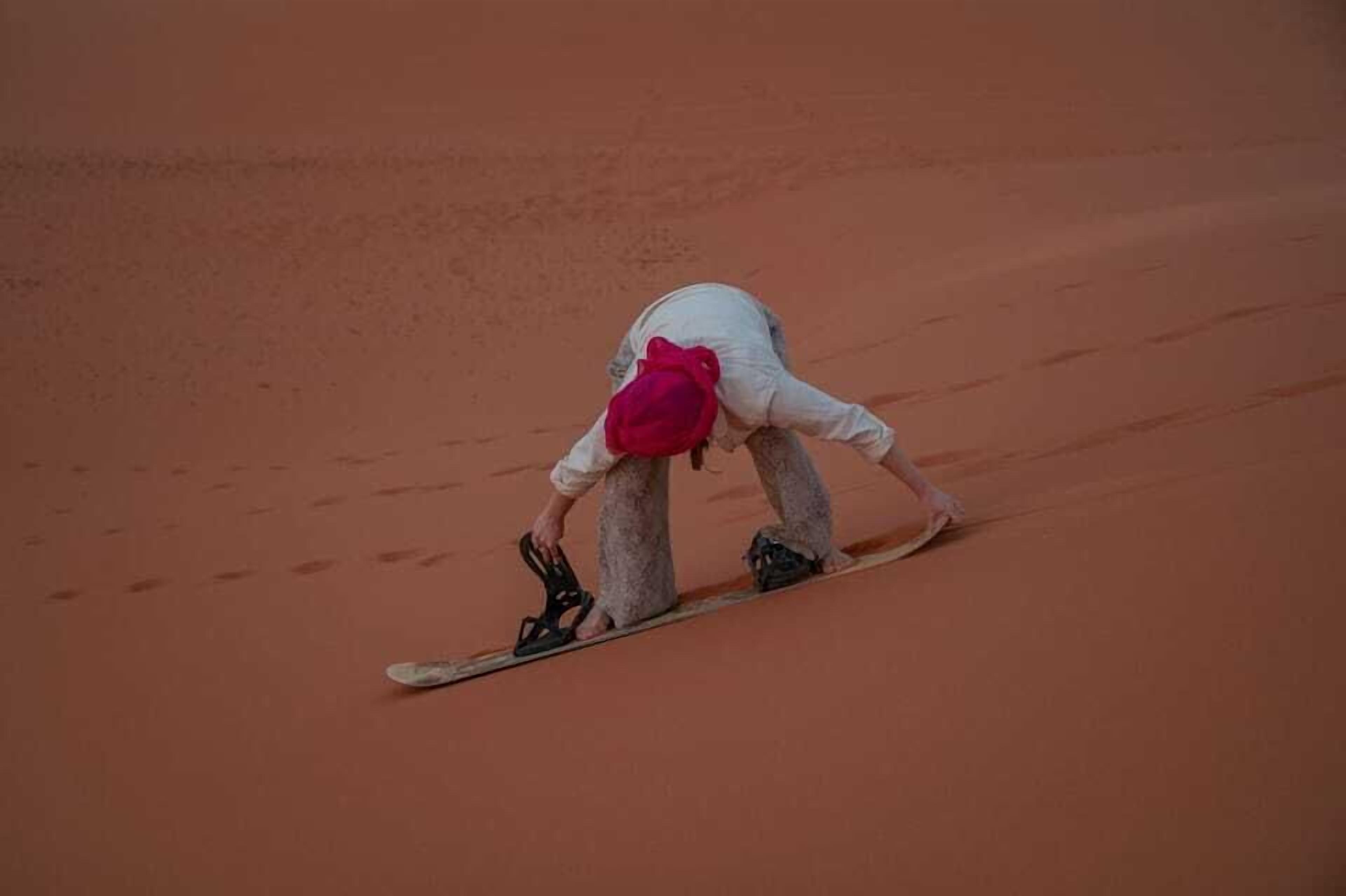 A person in white and red attire descending a sandy slope.