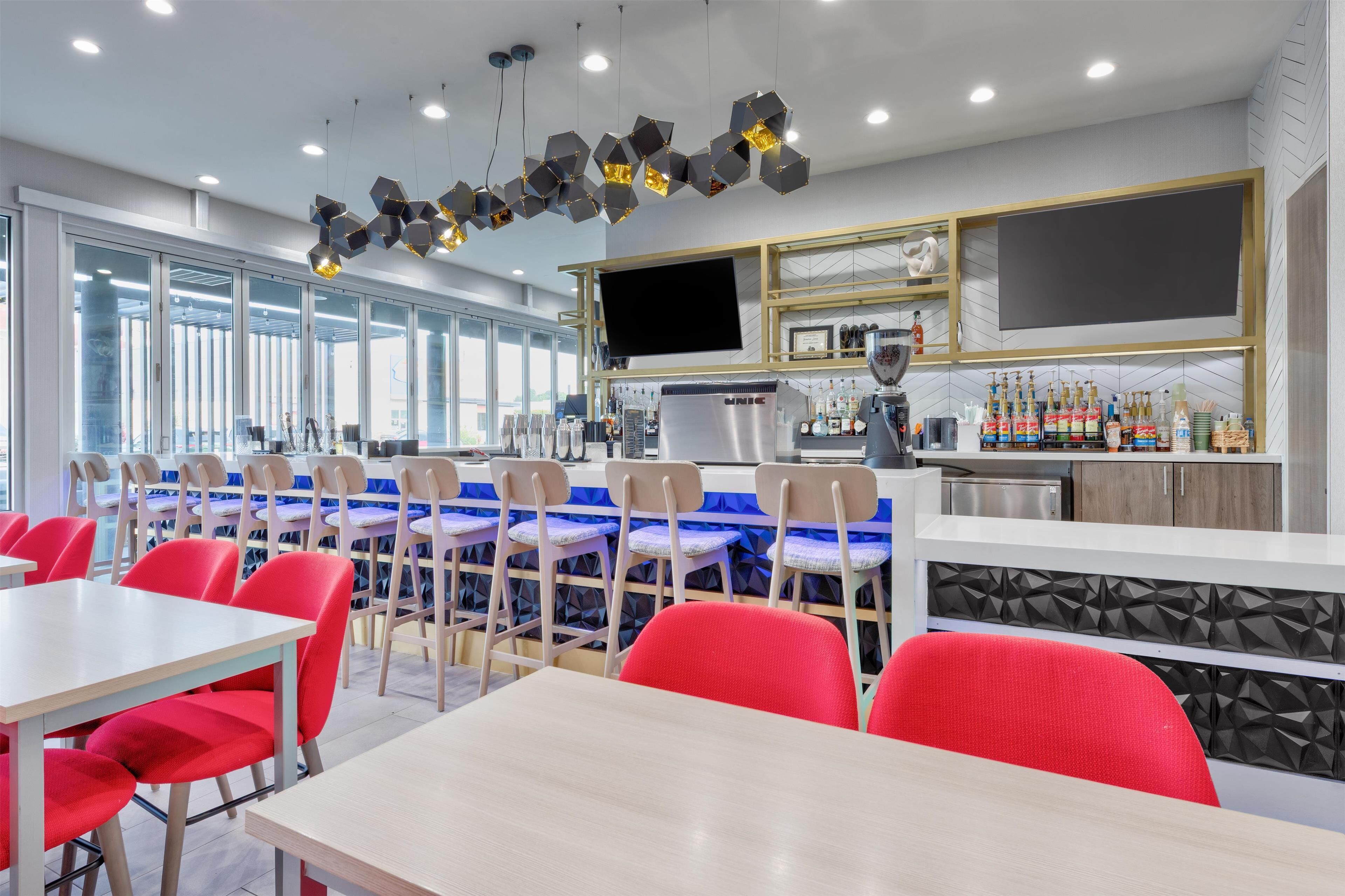 Un restaurante moderno con zona de bar, asientos con sillas rojas y una gran pantalla de televisión sobre la barra.