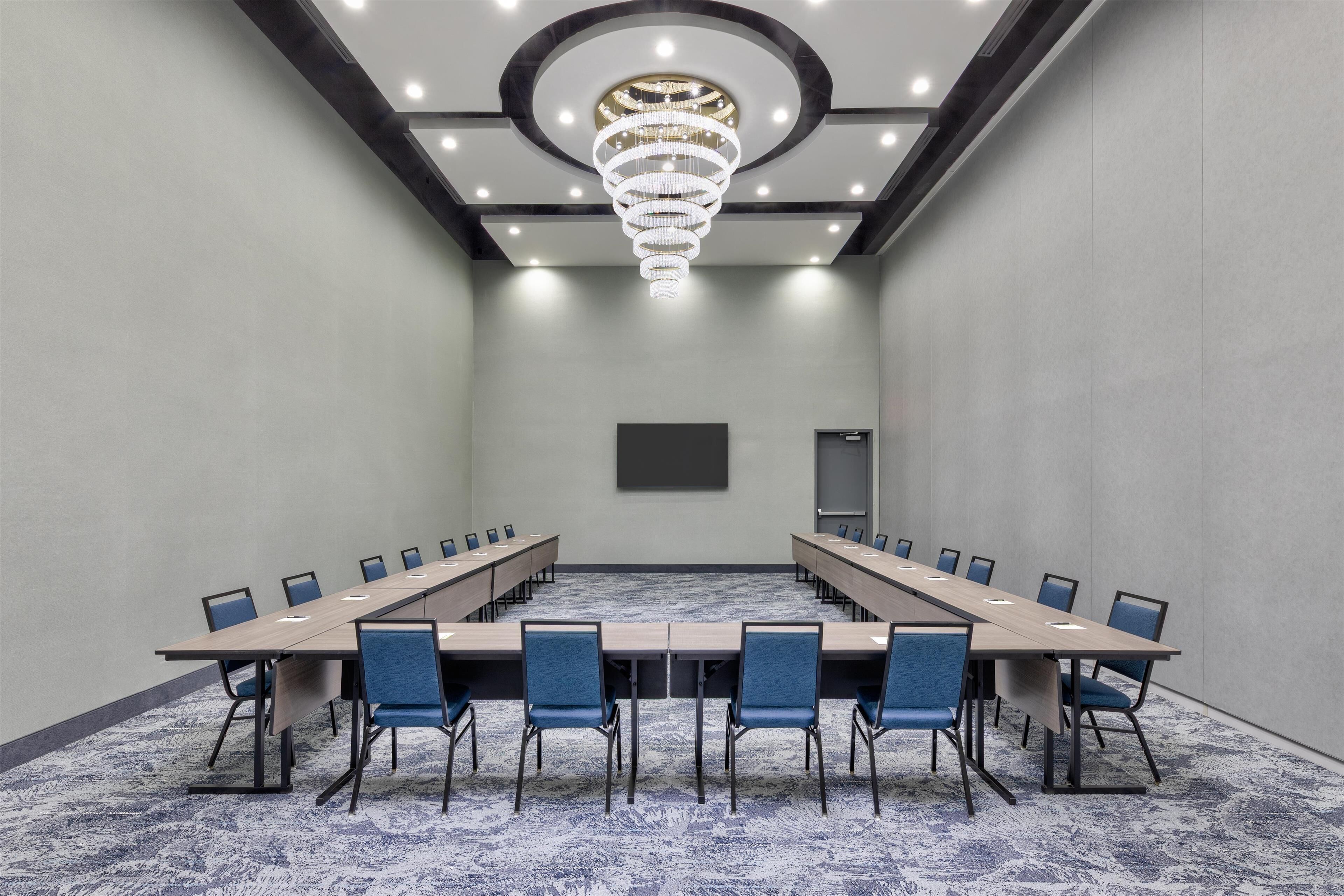 A conference room with a long table, blue chairs, a chandelier, and a projector screen.