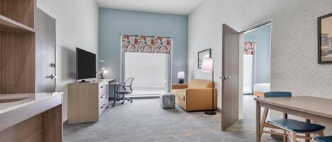 A modern hotel room with a desk, chair, sofa, and a television.