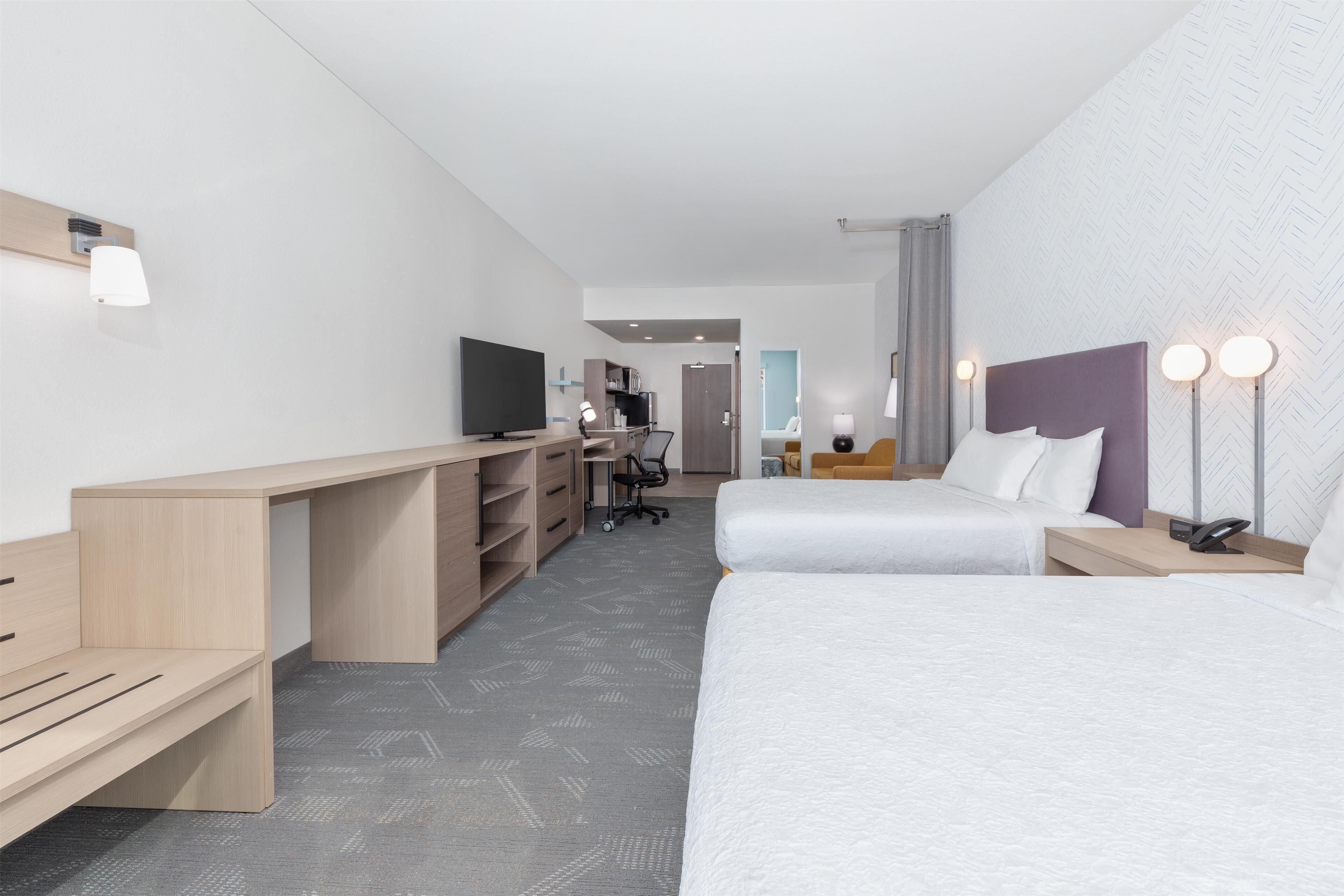Una habitación de hotel moderna con dos camas, un escritorio, un televisor y una pequeña zona de trabajo.